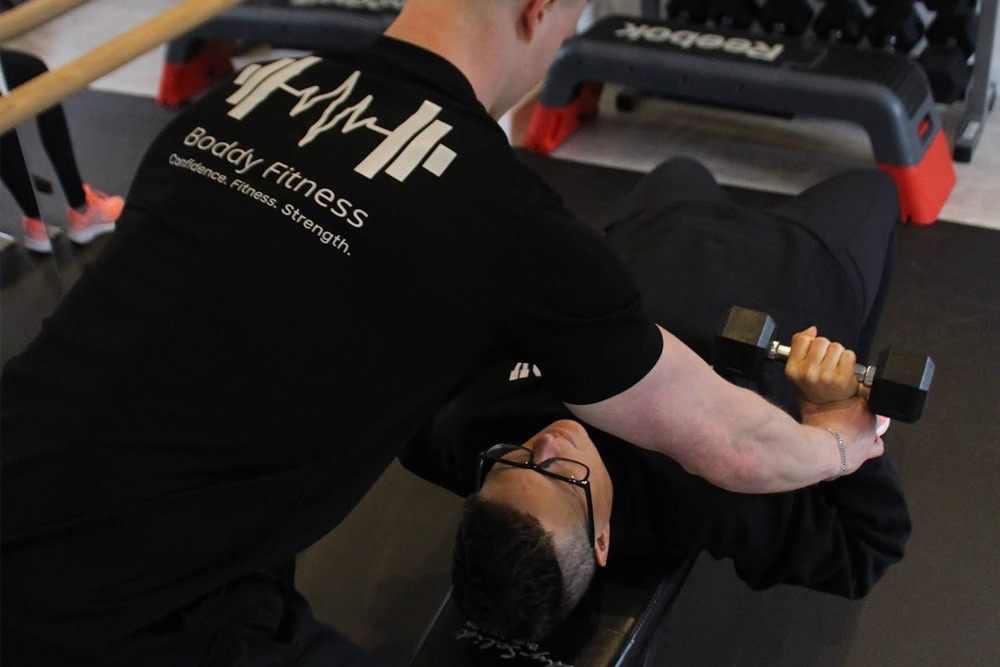 Personal trainer helping client with dumbbell exercises